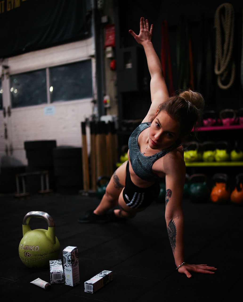 Fit woman doing a side plank exercise beside a kettleball and energy drink packs in a gym setting